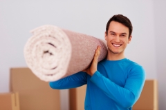 happy-male-carrying-carpet-new-home
